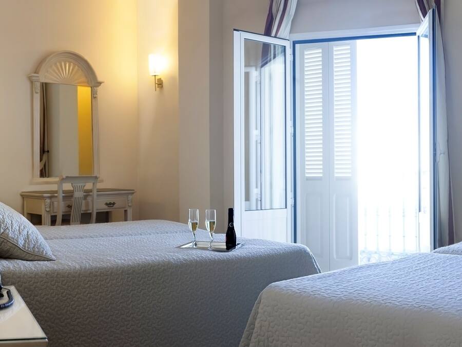 A hotel room with two beds, a desk with a phone and a glass of water, a chair, a table, a mirror, and a TV on the wall.