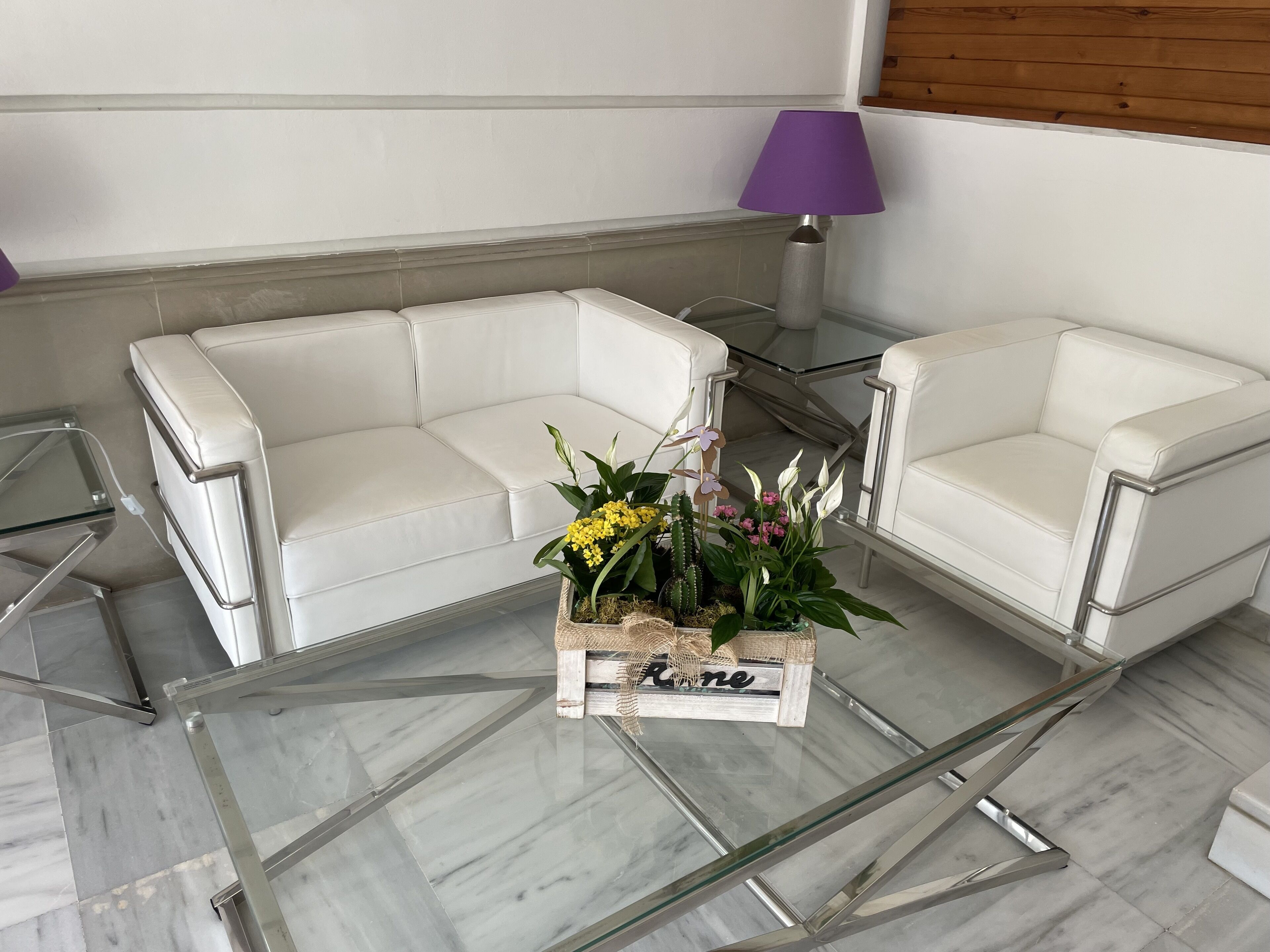 Uma sala de estar moderna com uma mesa de centro de vidro, sofás de couro branco e um abajur roxo.