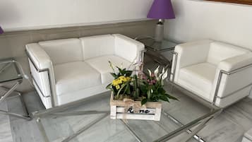 Uma sala de estar moderna com uma mesa de centro de vidro, sofás de couro branco e um abajur roxo.
