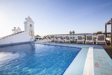 Una piscina al aire libre, sombrillas, sillones reclinables de piscina