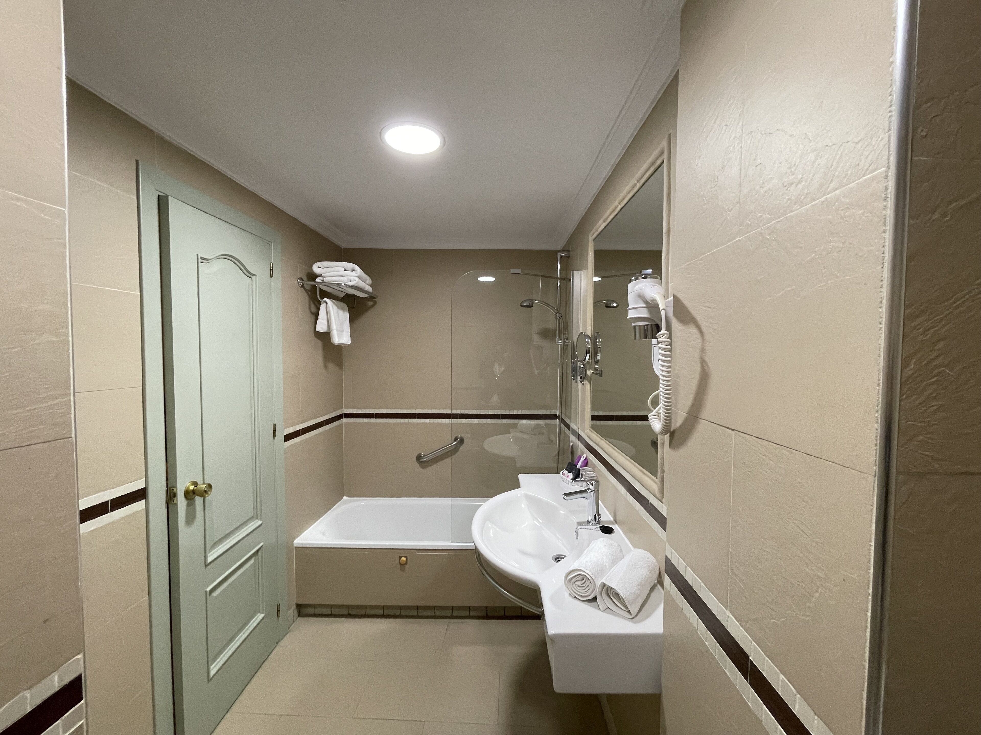 A bathroom with a bathtub, a sink, a mirror, and a hairdryer.