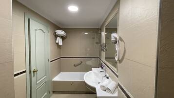 A bathroom with a bathtub, a sink, a mirror, and a hairdryer.