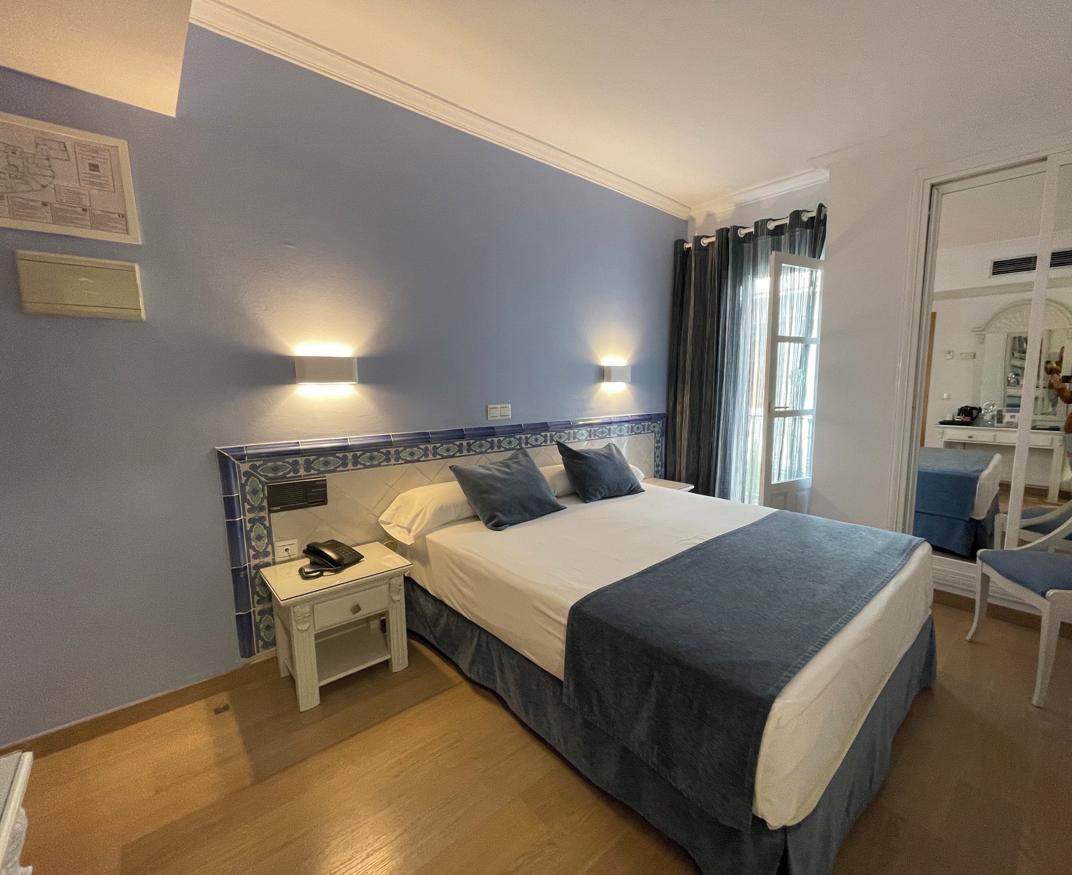Una habitación de hotel con una cama grande, una mesita de noche con teléfono y una silla.
