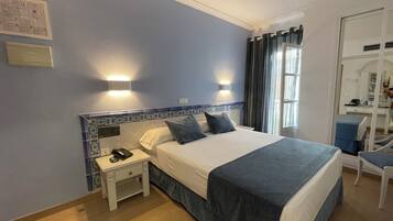 Una habitación de hotel con una cama grande, una mesita de noche con teléfono y una silla.