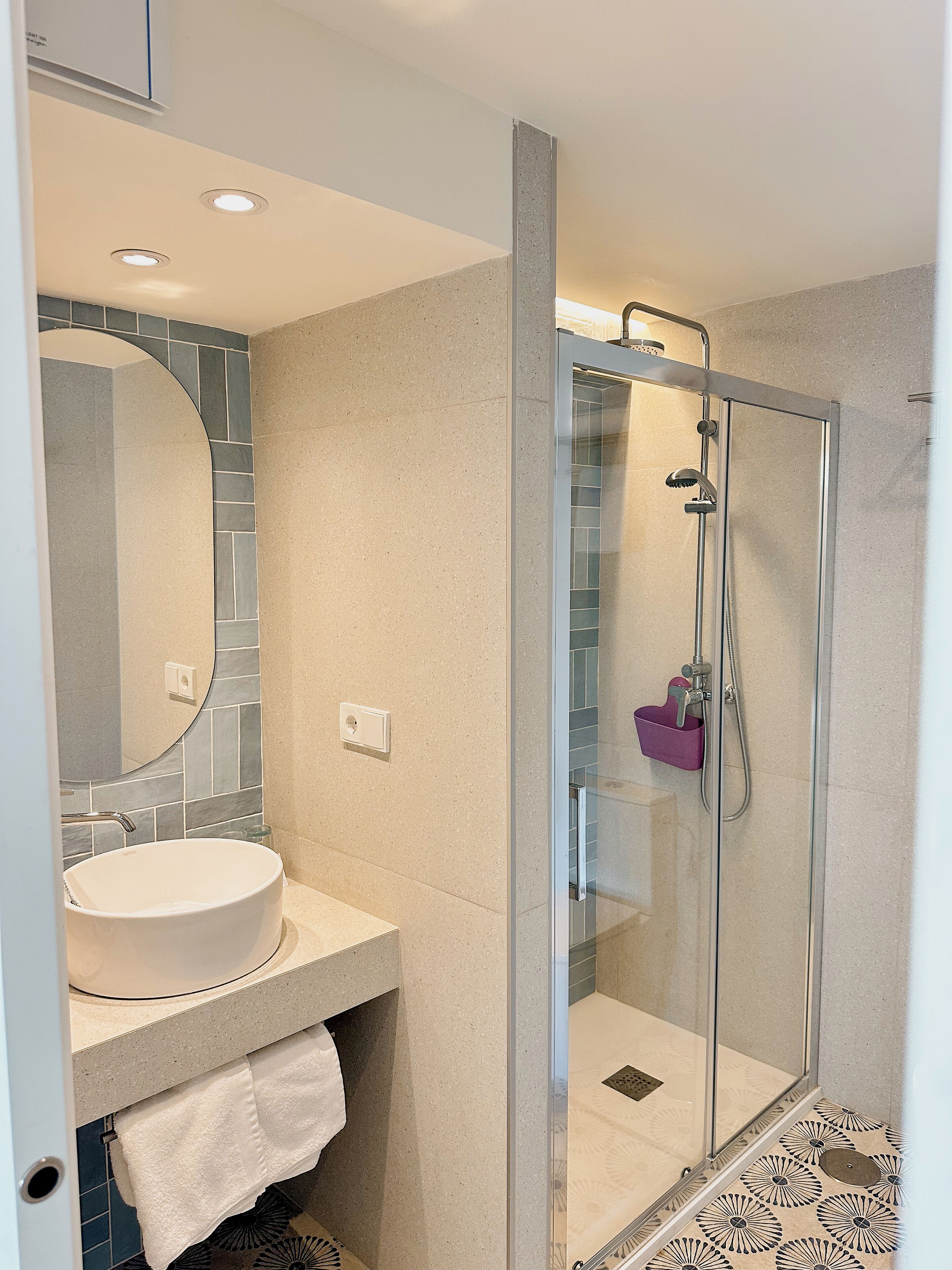 Une salle de bain moderne avec une douche à parois de verre, un miroir rond et un lavabo blanc.
