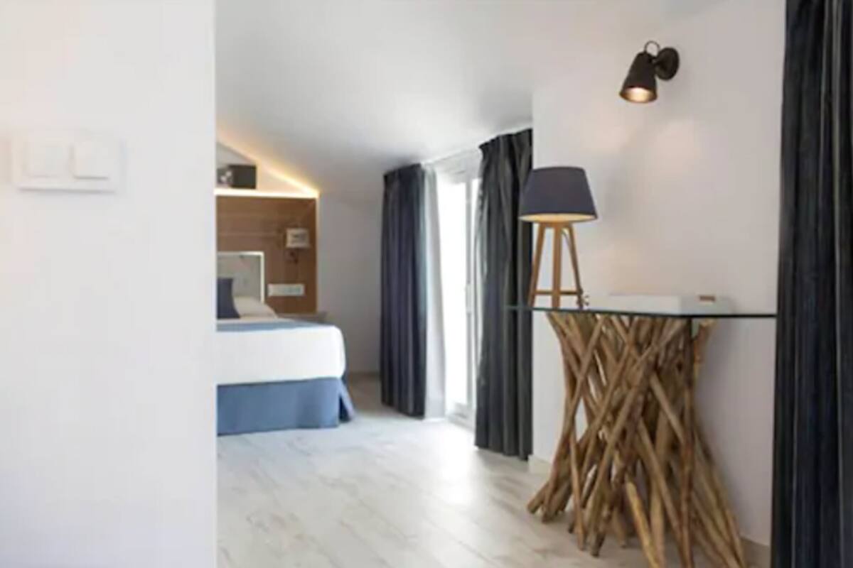 Una habitación de hotel moderna con una cama, un escritorio con lámpara y una base de mesa de madera original.