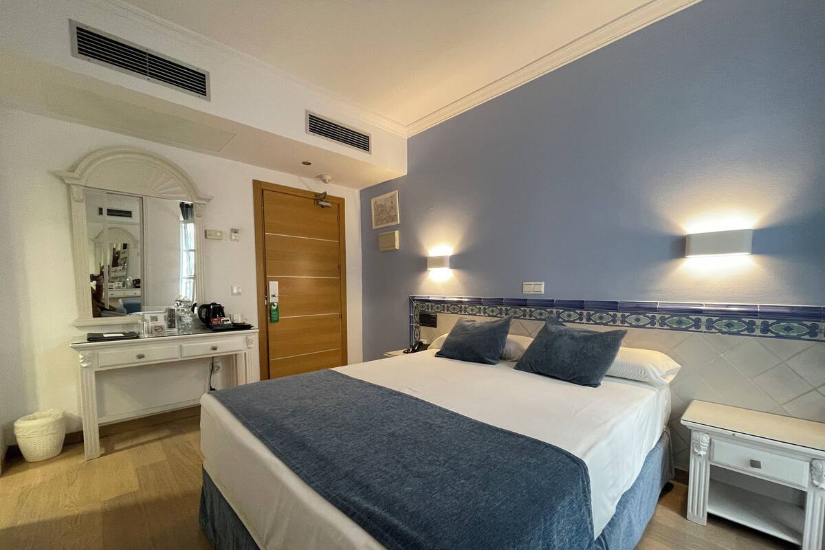 Habitación de hotel con cama, mesita de noche, tocador y armario.