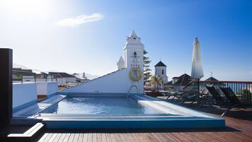 A rooftop pool with a clock tower, lounge chairs, and a wooden deck.