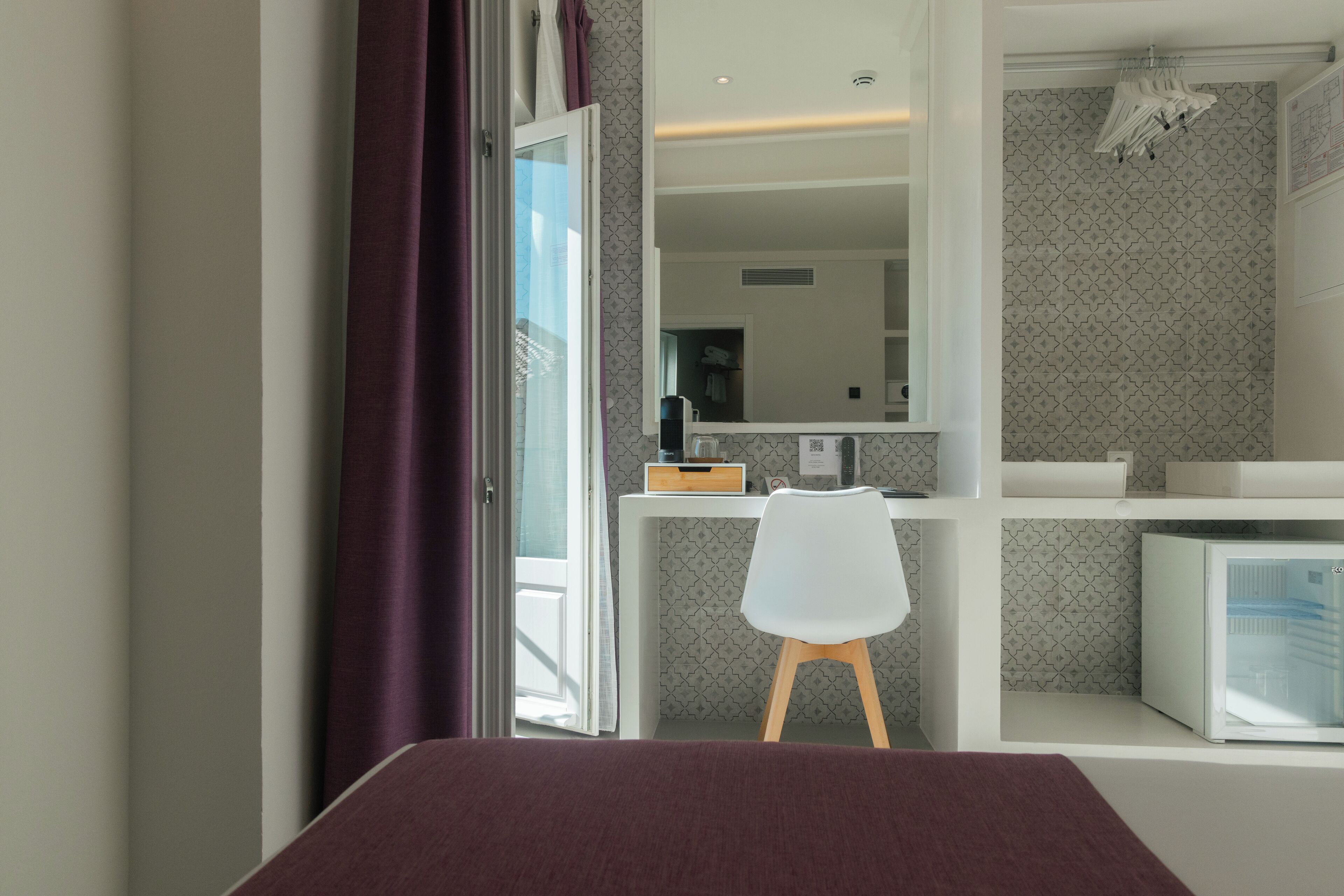 Una habitación moderna con una cama, un escritorio con silla, un espejo y un refrigerador.