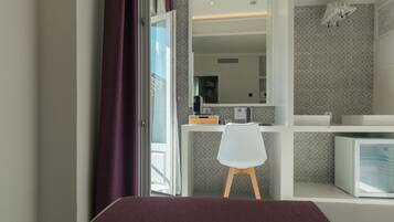 Una habitación moderna con una cama, un escritorio con silla, un espejo y un refrigerador.