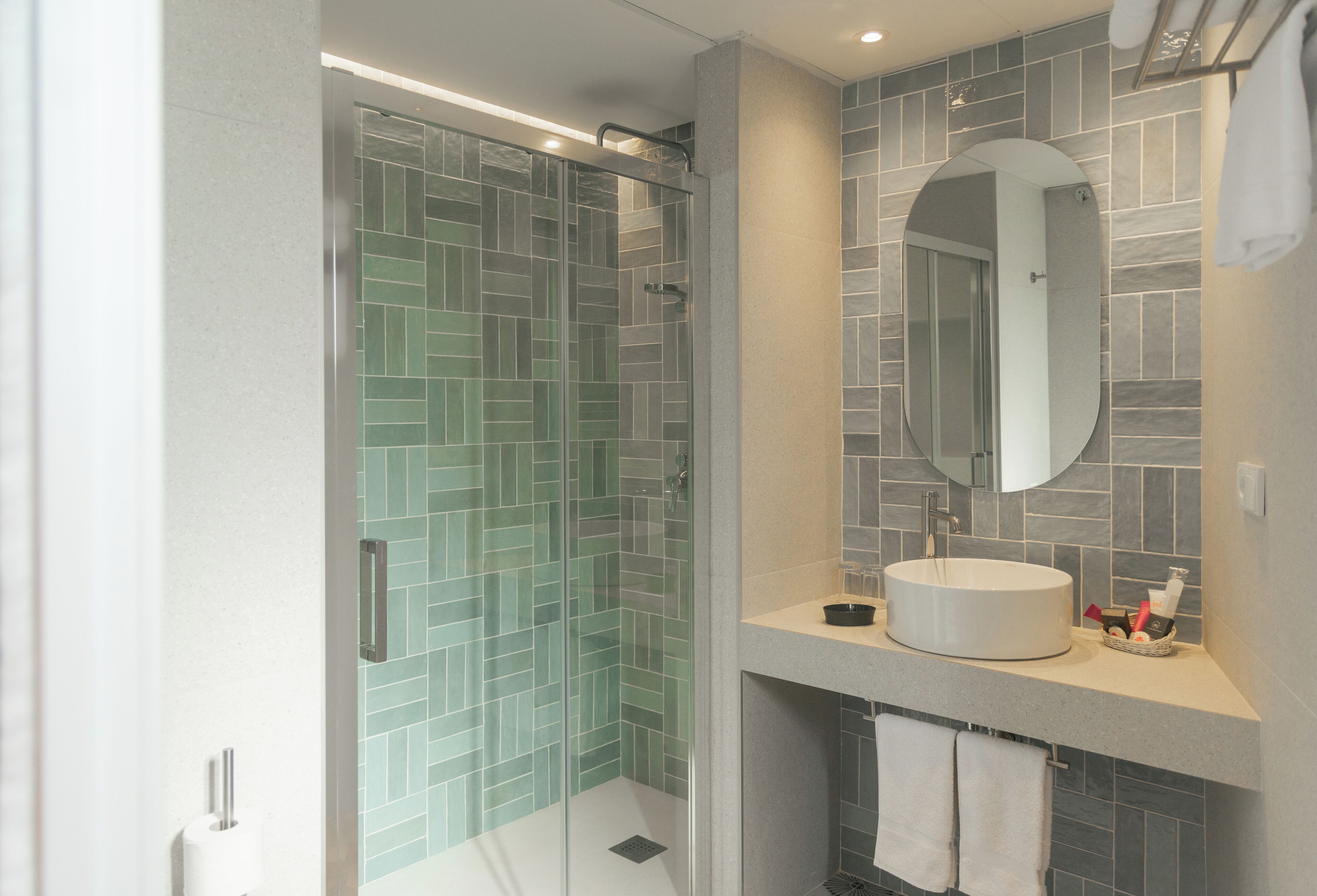 A modern bathroom with a glass-enclosed shower, a round mirror, and a sink with toiletries.