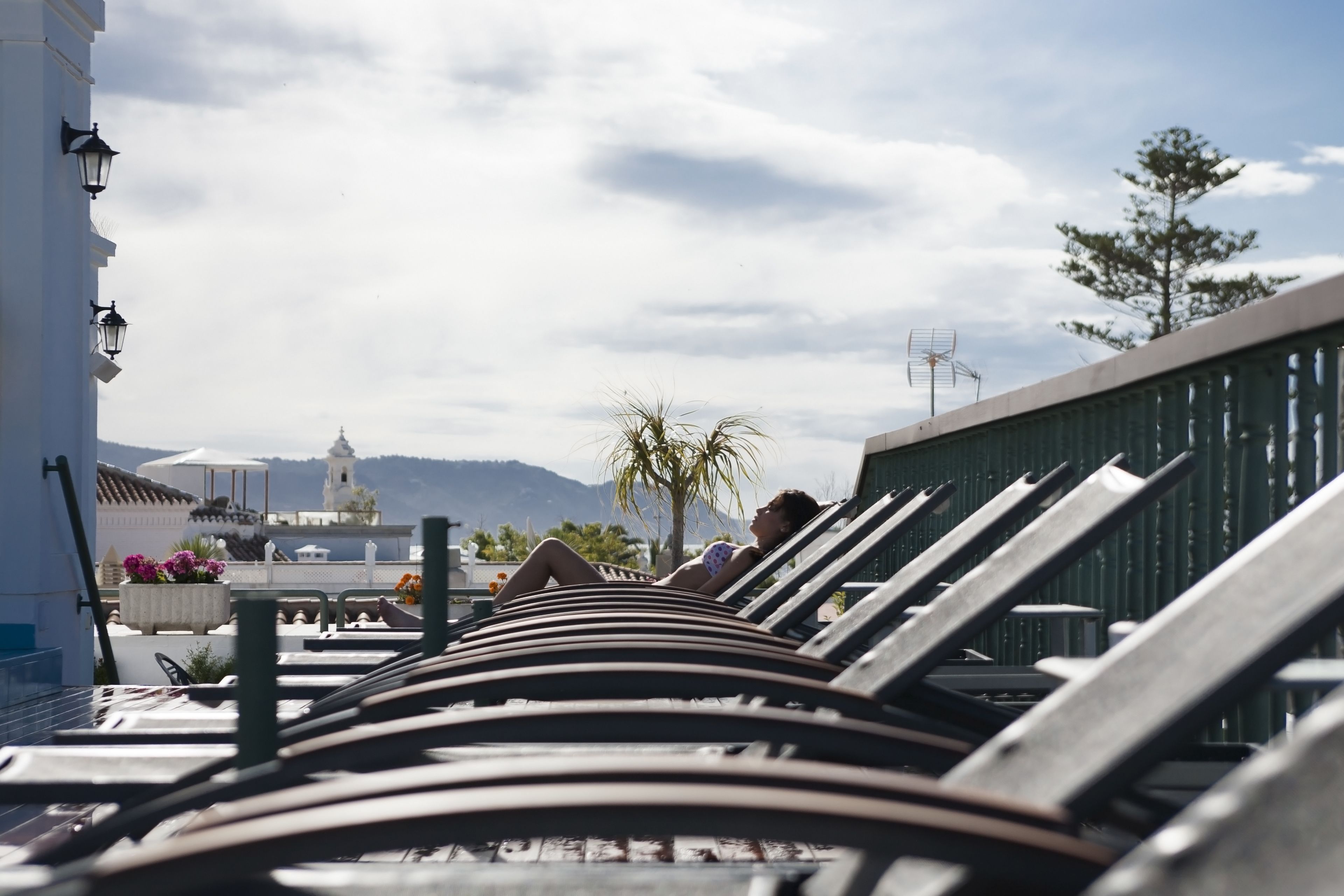 Une rangée de chaises longues, avec vue sur un bâtiment blanc et des montagnes en arrière-plan.