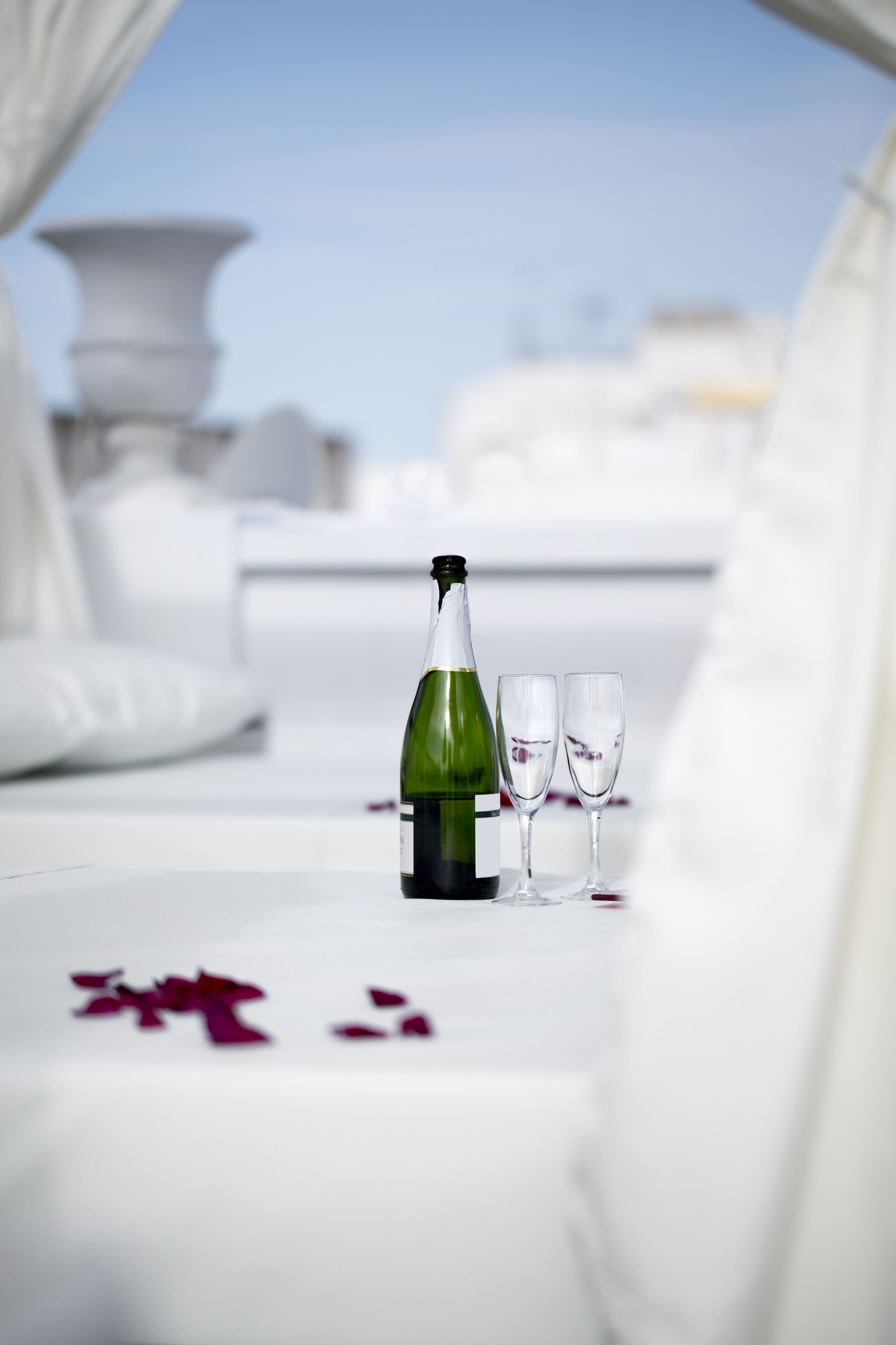 Une table avec une bouteille et deux verres, disposés sur une surface blanche parsemée de pétales de rose.