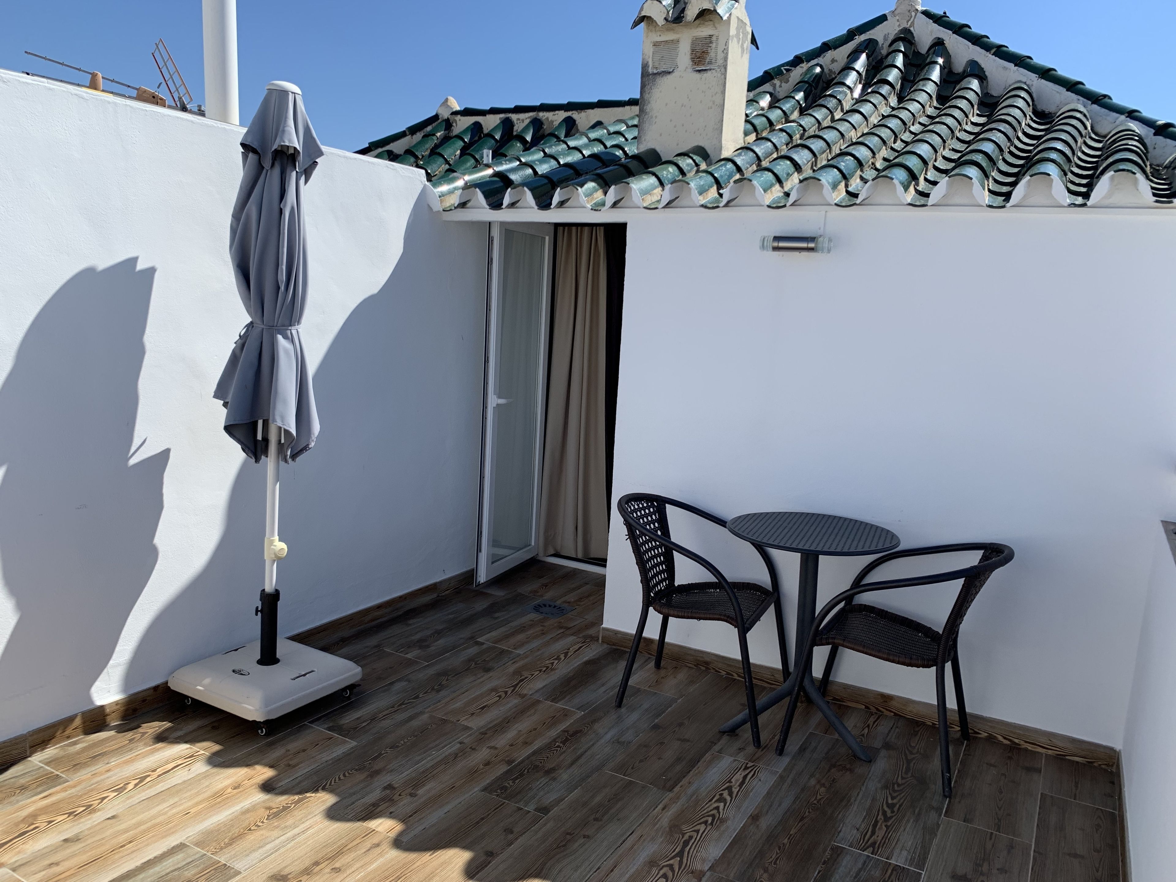 Een klein terras met een tafel, stoelen, een weegschaal en een overdekte parasol.