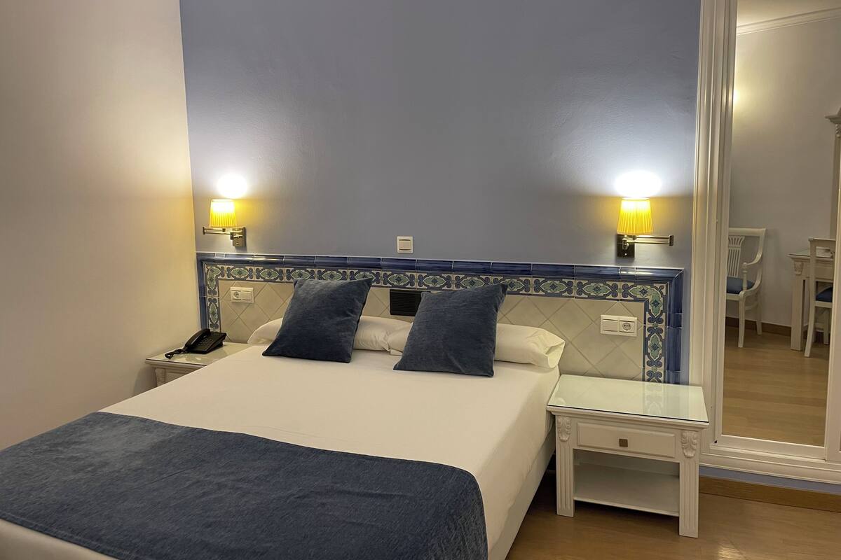 Habitación de hotel ordenada con cama, mesitas de noche y un espejo grande.