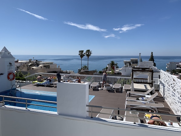 Zona de piscina con sillones y vista al mar.