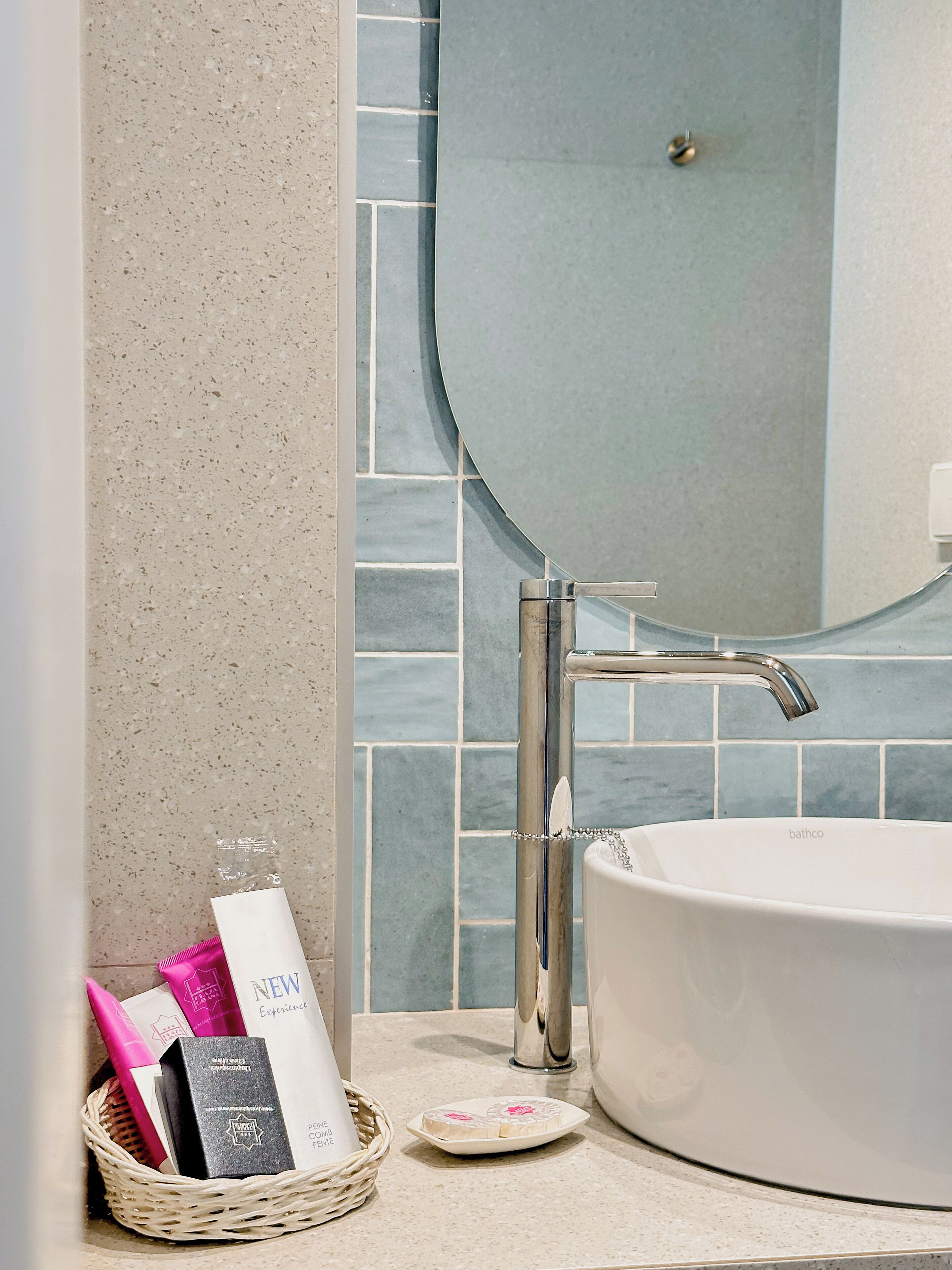 A bathroom with a white sink, a chrome faucet, and a mirror. There is a basket with toiletries and a soap dish on the countertop.