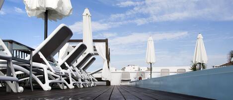 A wooden deck with lounge chairs and white umbrellas, overlooking a pool area.