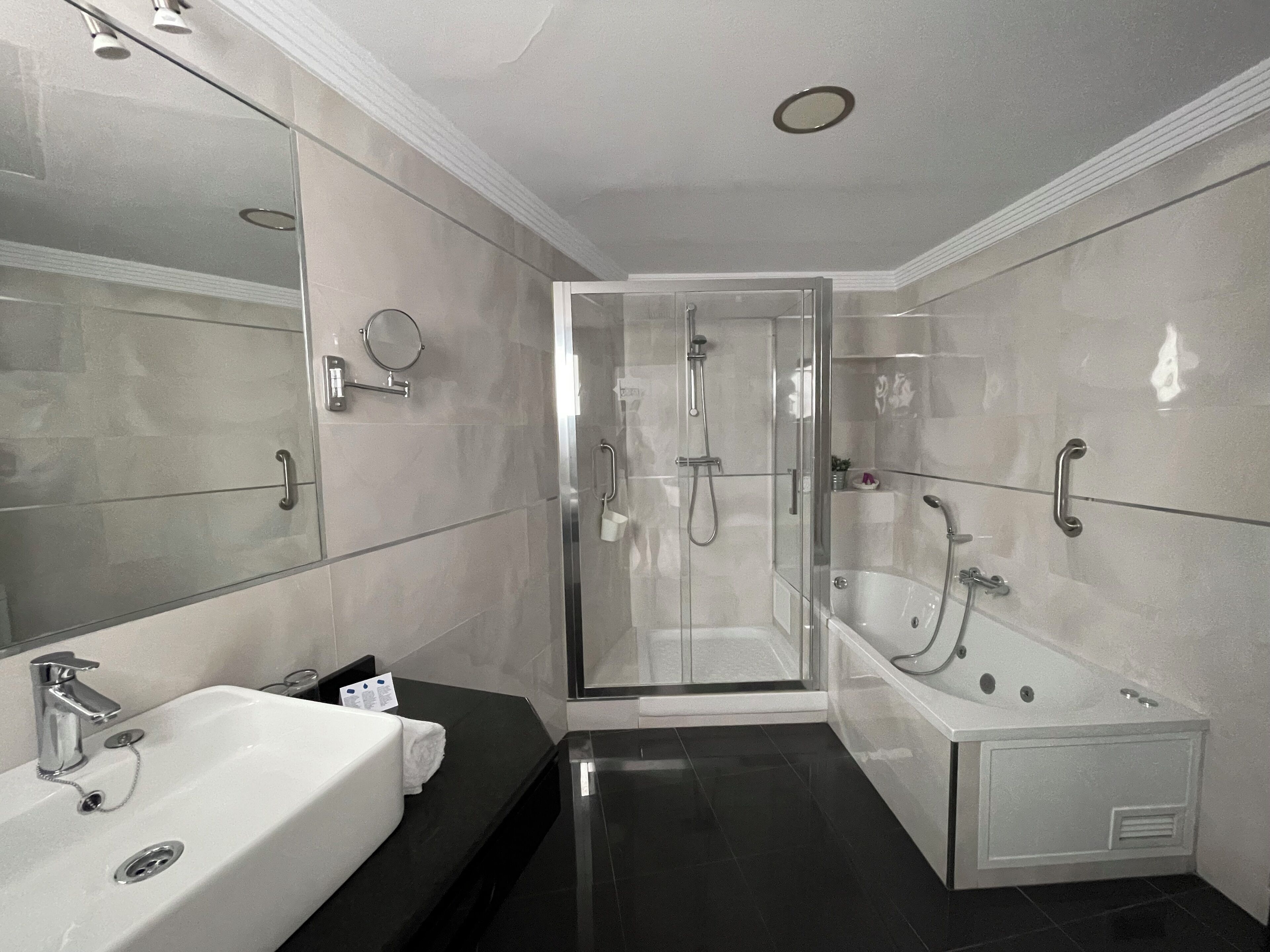 A modern bathroom with a large mirror, a white bathtub, and a glass-enclosed shower area.