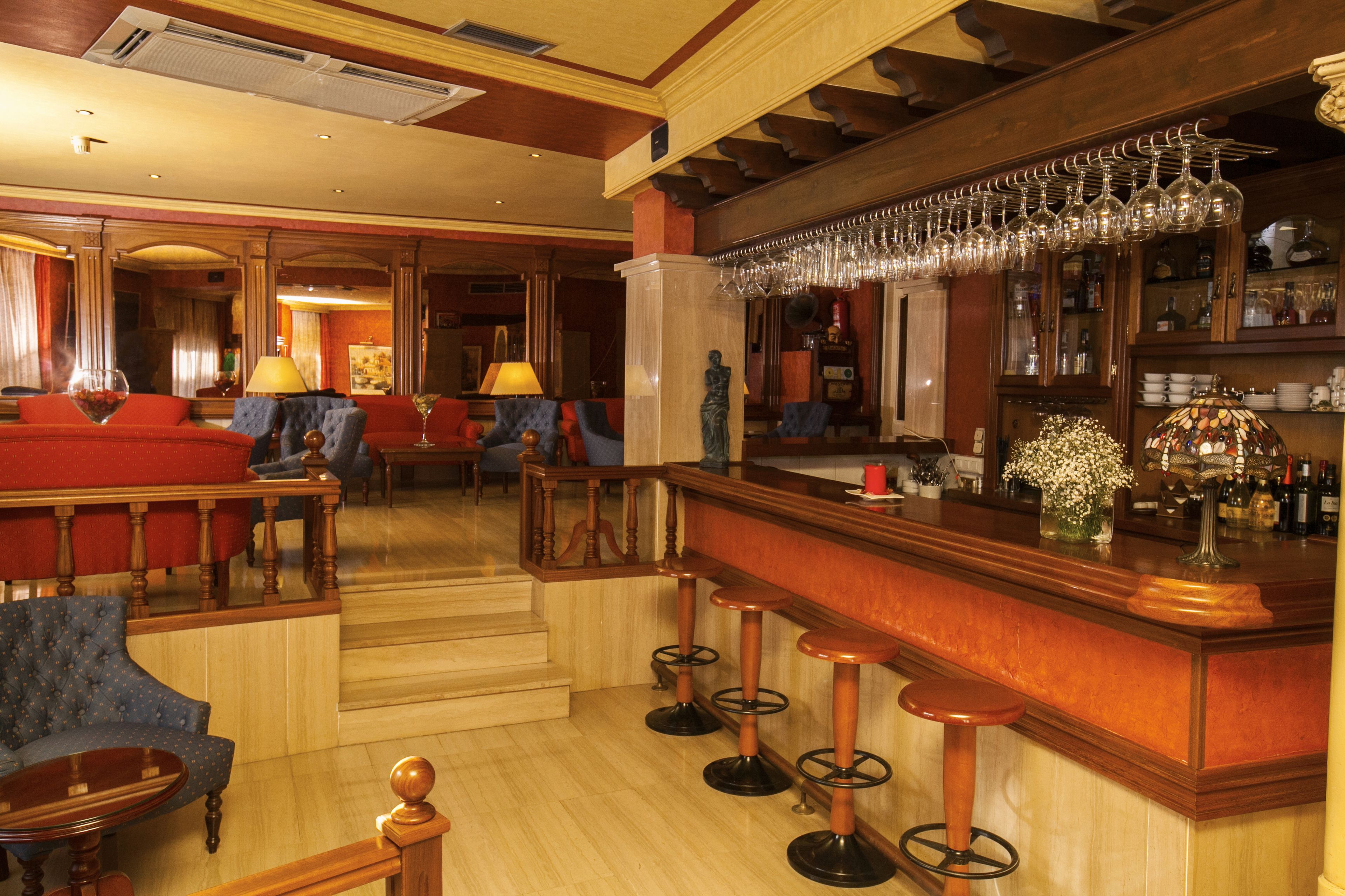 Zona de bar con taburetes, barra y una estantería para vinos con copas.