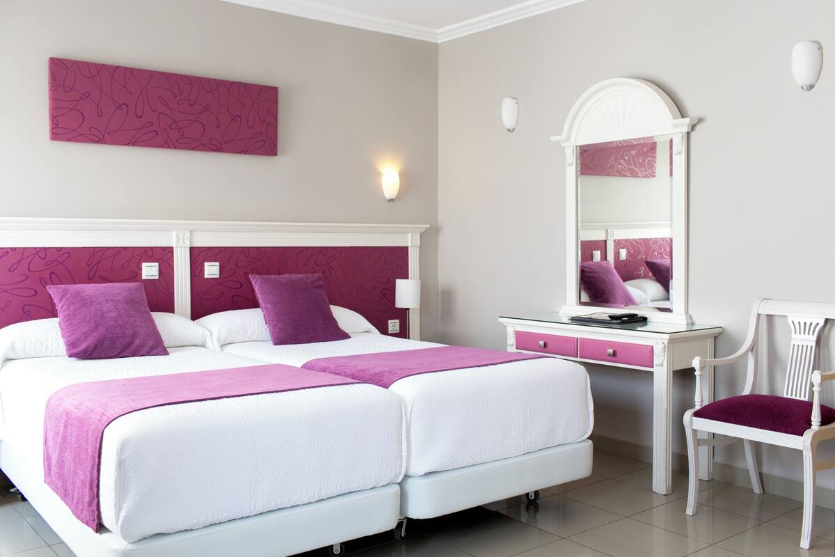 Una cama doble con dos almohadas, una mesita de noche, una silla y un espejo.