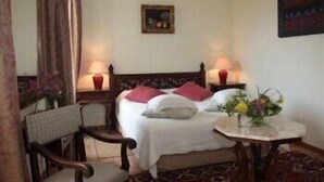 Une chambre d’hôtel avec un lit, deux lampes de chevet, une chaise, une petite table sur laquelle est posé un vase de fleurs, et un tableau au mur.