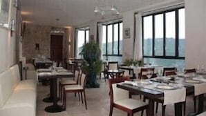 Un espace repas avec des tables dressées pour les repas, de grandes fenêtres offrant une vue et une plante au centre.
