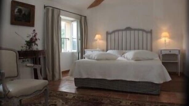 Une chambre à coucher avec un lit, deux tables de chevet, une chaise et une fenêtre avec des rideaux.