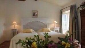 Une chambre avec deux lits, une grande fenêtre avec des rideaux et une table de chevet avec une lampe.