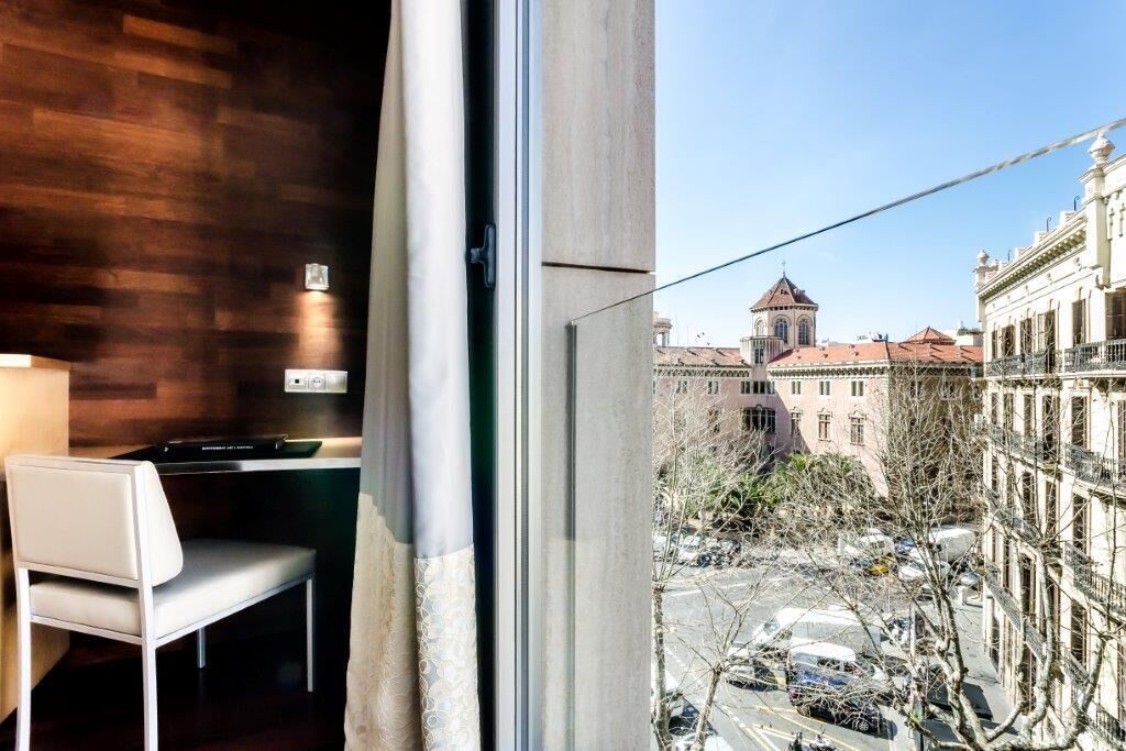 A room with a view of a cityscape, a window, and a chair.
