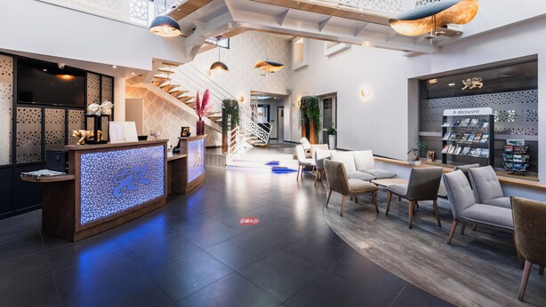 A modern hotel lobby with a reception desk, seating area, staircase, and a large window displaying a sign. - The Originals Boutique, Hôtel Le Lion d'Or (Maen-Roch)