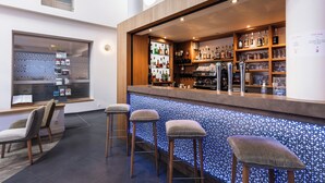 A bar area with stools, a counter, and shelves of bottles. - The Originals Boutique, Hôtel Le Lion d'Or (Maen-Roch)