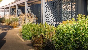 A covered outdoor area with a modern architectural design, featuring a patterned metal fence and various green shrubs. - The Originals Boutique, Hôtel Le Lion d'Or (Maen-Roch)