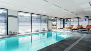 A modern indoor swimming pool with clear glass walls, lounge chairs, and a tiled floor. - The Originals Boutique, Hôtel Le Lion d'Or (Maen-Roch)