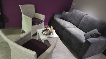 Un espacio de estar con un sofá gris, un sillón de mimbre y una pequeña mesa con un adorno.