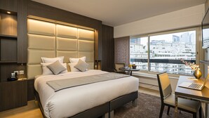 A modern hotel room with a large bed, a desk with a laptop, and a view of the city through large windows. - Residhome Courbevoie La Défense (Courbevoie)