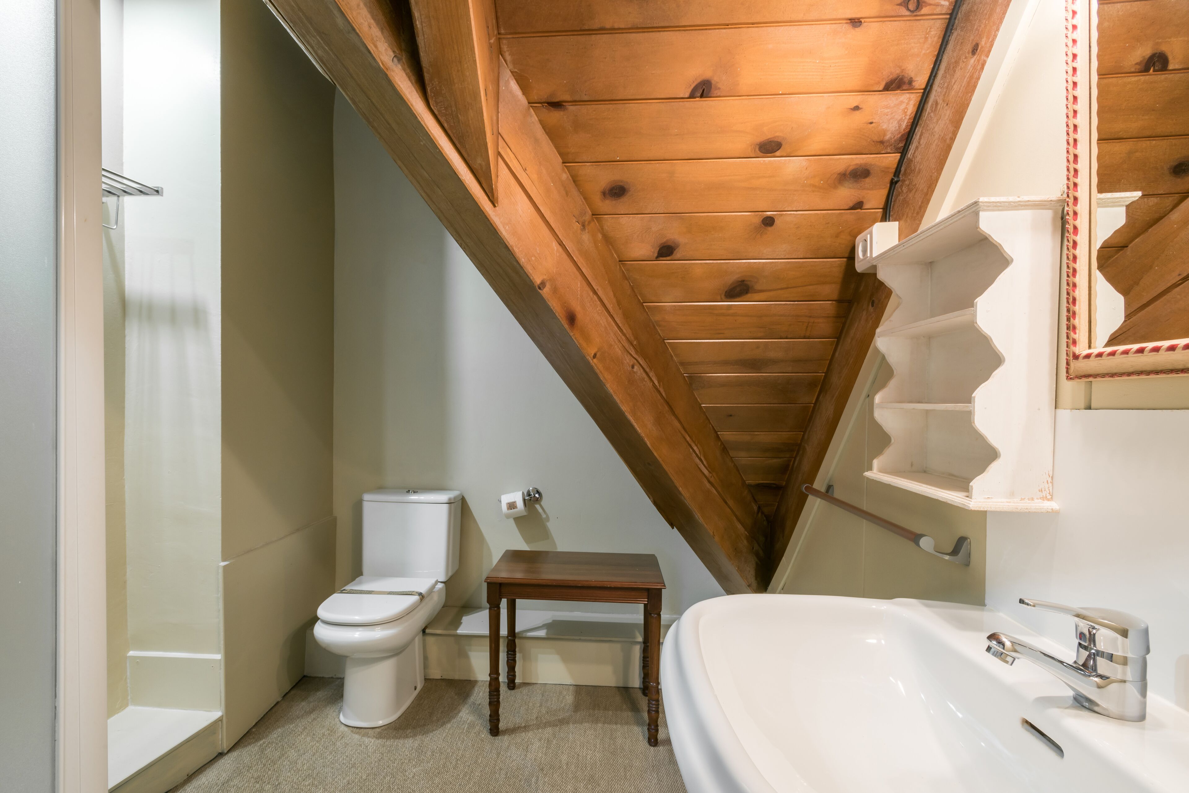 A bathroom with a wooden ceiling, a toilet, a small wooden table, and a sink.