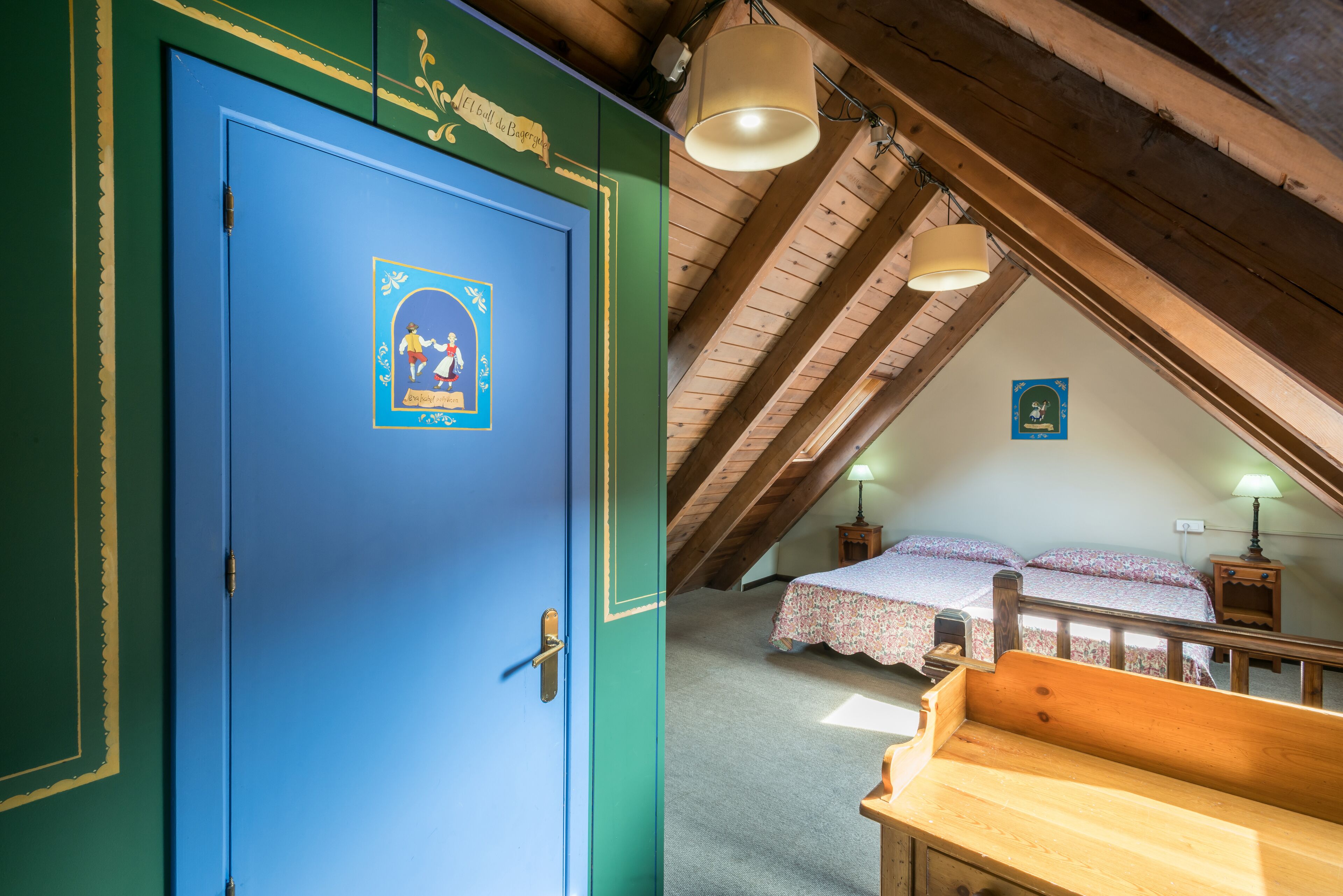 Una habitación con una puerta azul, un banco de madera, una cama con ropa de cama floral y un techo inclinado con vigas de madera.