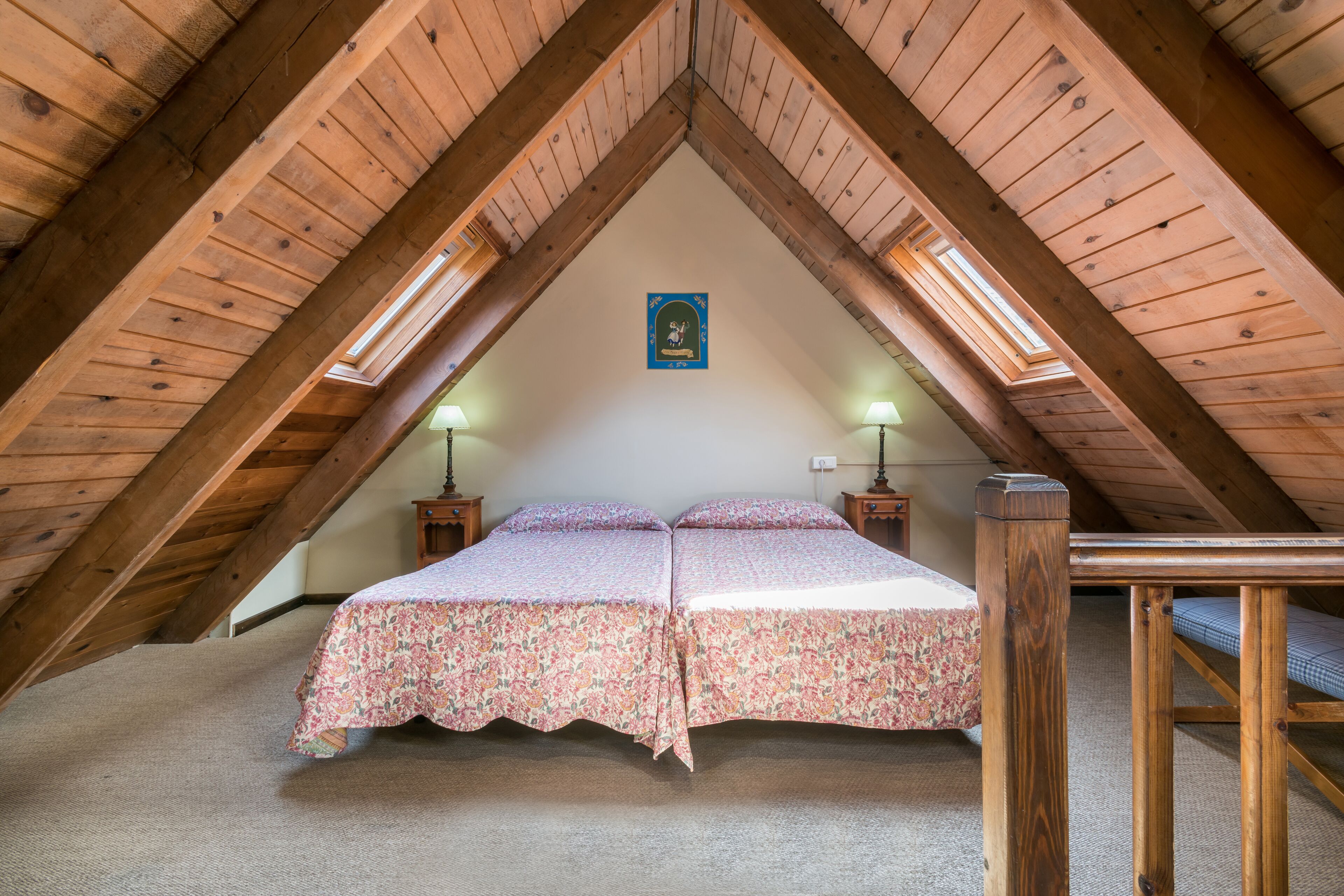 A bedroom with two beds, wooden beams, skylights, and a small table.