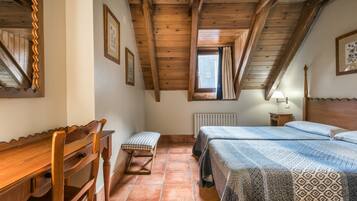 A bedroom with wooden beams, a desk, two beds, a radiator, and a window with curtains.