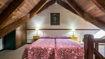Un dormitorio con techo inclinado, vigas de madera, dos mesitas de noche con lámparas y una cama con ropa de cama floral.