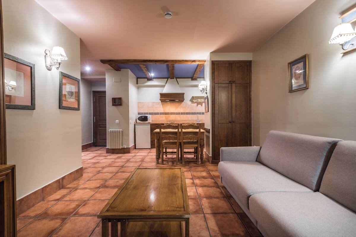 A living room with a sofa, a wooden coffee table, and a kitchen area with a dining table and chairs.