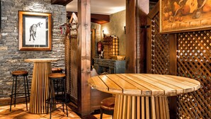A rustic interior with a wooden table and stools, a stone wall with a framed picture, and a wooden lattice partition. - El Refugio de Aran Vielha Aparthotel (Vielha e Mijaran)
