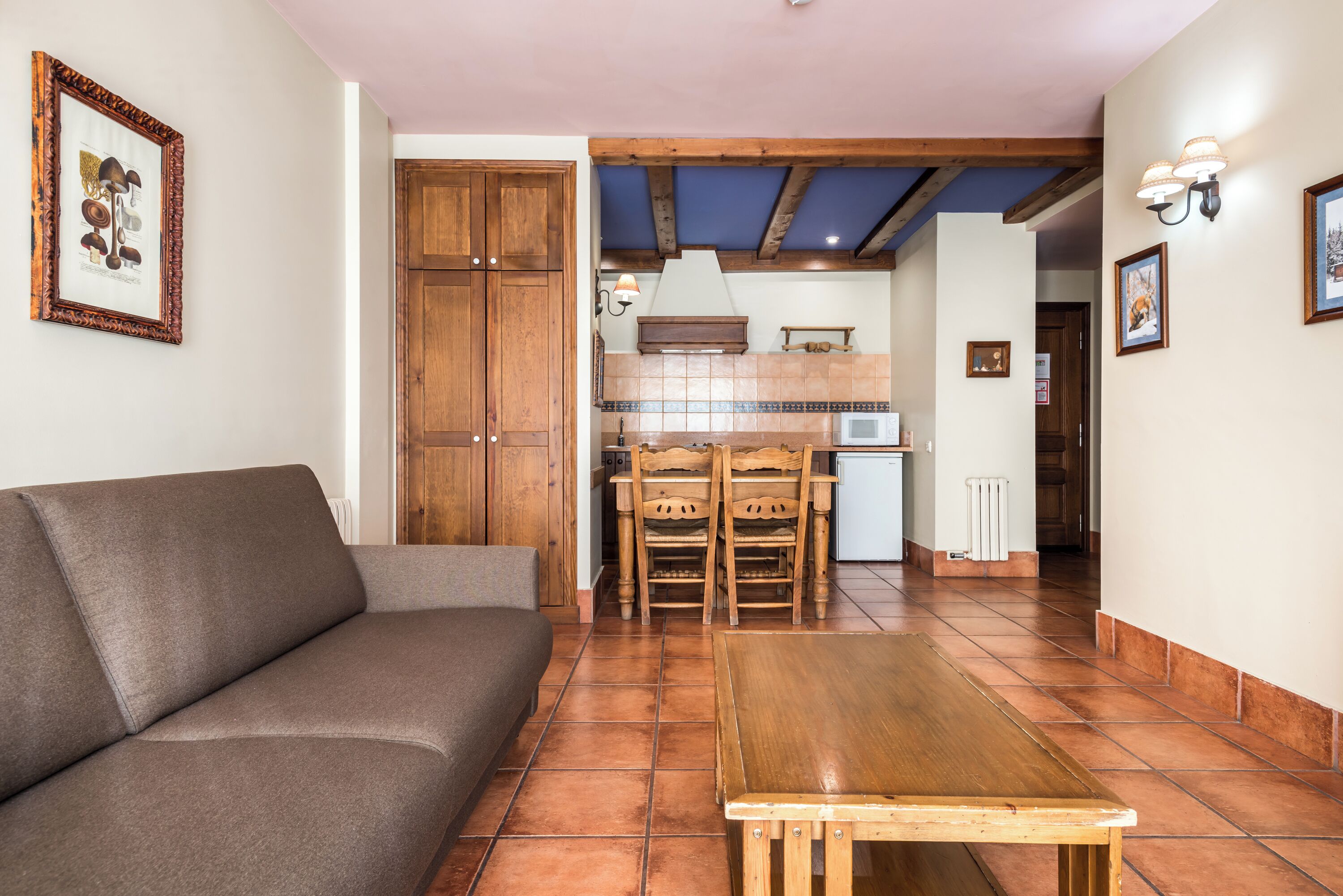 Una sala de estar con sofá, una mesa de madera y una cocina al fondo.