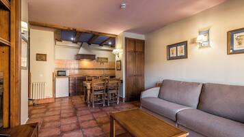 A cozy living room with a sofa, a wooden coffee table, and a kitchen area with a dining table and chairs.