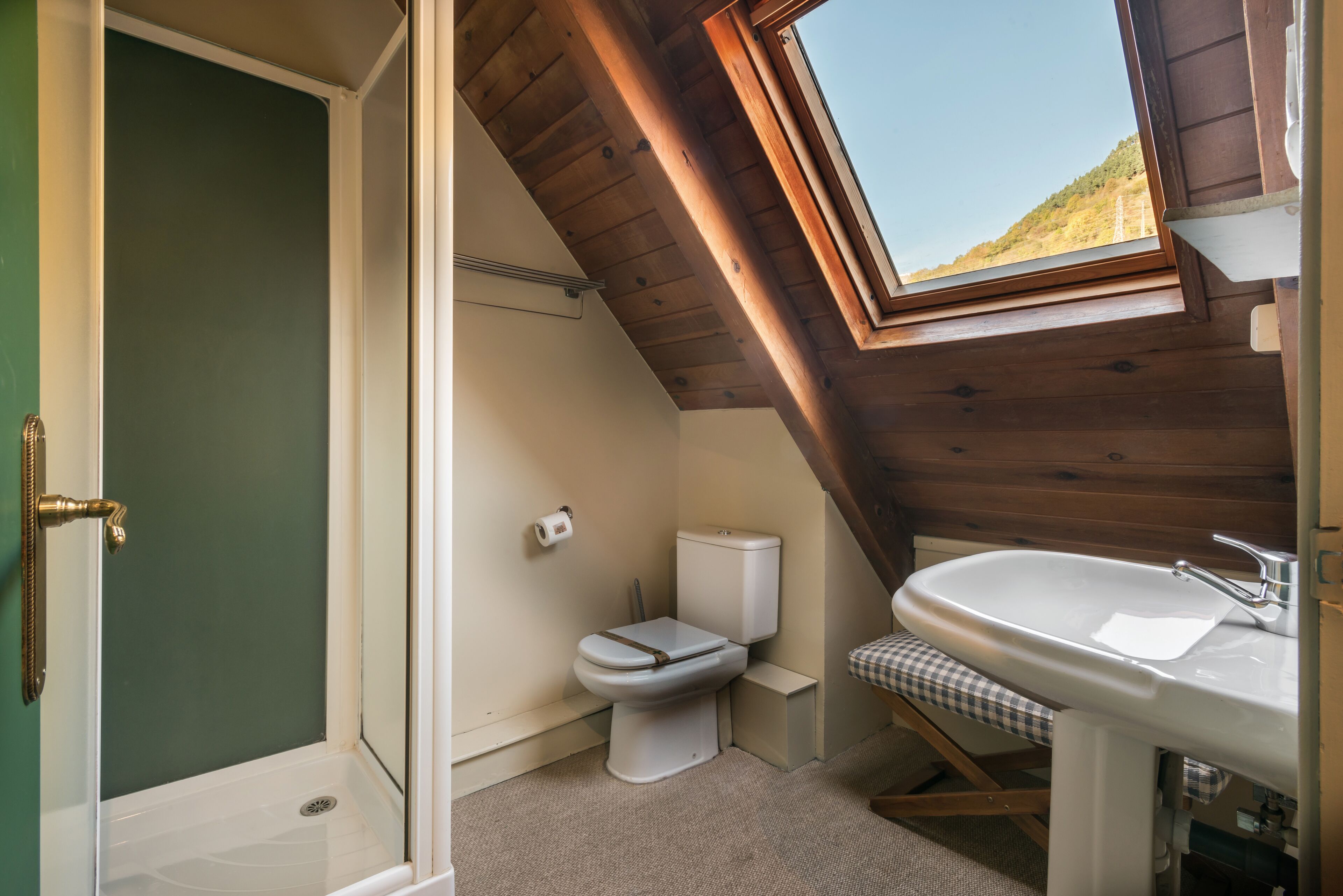 A small, sloped-roofed bathroom with a toilet, sink, and shower.