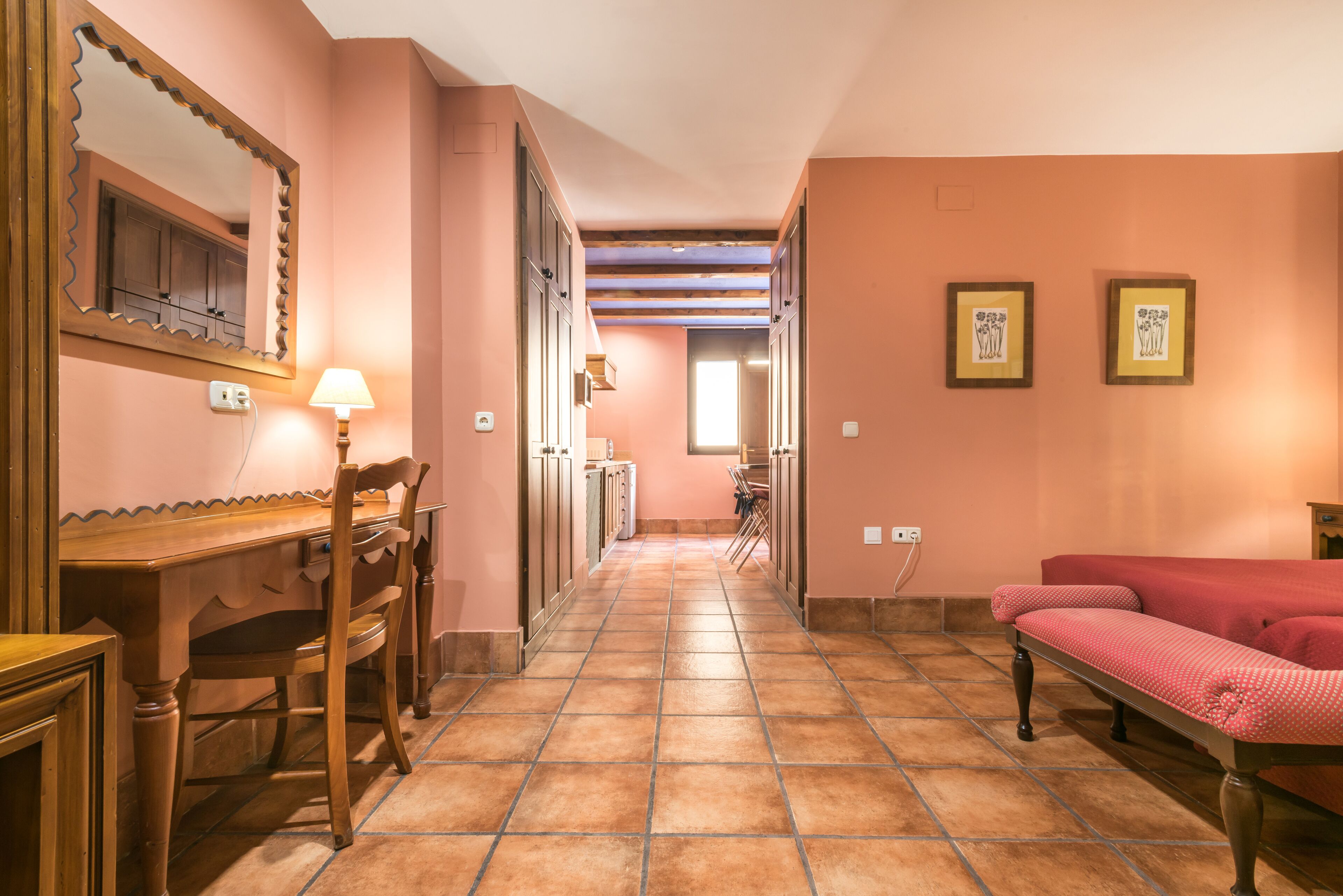 A hallway with a wooden desk, chairs, a red sofa, and framed pictures on the walls.