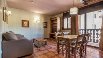 A cozy living area with a sofa, a dining table with chairs, a small coffee table, and a bookshelf.