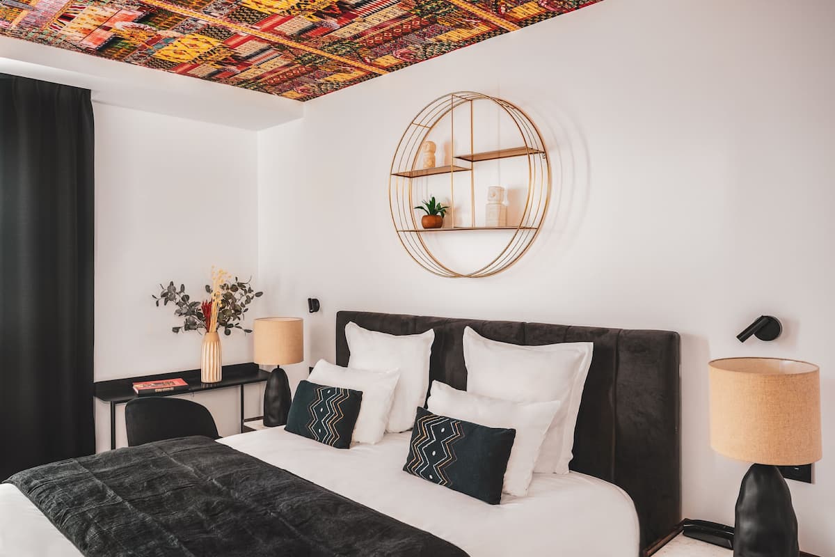 Una habitación de hotel moderna con una cama grande, un estante redondo en la pared y un techo con un diseño colorido.