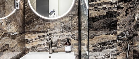 Un baño moderno con salpicadero de mármol, un espejo redondo, un lavabo blanco y una bañera.